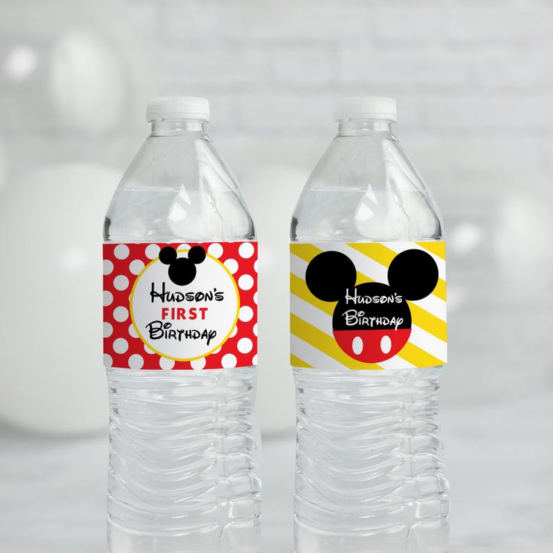 May include: Two clear plastic water bottles with personalized labels for a birthday party. The labels feature a red and white polka dot pattern with a yellow circle and Mickey Mouse ears on one bottle and a yellow and black striped pattern with a red Mickey Mouse head on the other. The text on the labels reads "Hudson's First Birthday".
