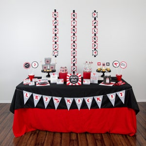 May include: A black and red table with a red tablecloth and a black and white banner that says "Let's Kick It". The table is decorated with a karate-themed birthday party decorations, including a sign that says "Alex's Dojo", black and red paper lanterns, and black and red paper cups.