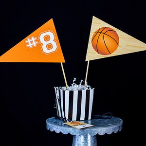 May include: Two orange and white pennants with the number 8 and a basketball design, a black and white striped container, and a small silver cake stand with a tag that says "MVP Party".