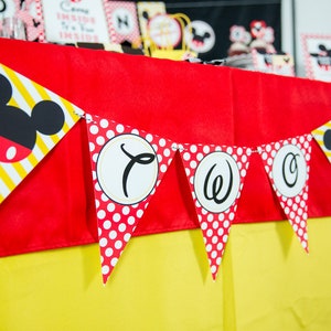 May include: A festive banner with Mickey Mouse-themed pennants. The pennants feature a mix of red polka dots, yellow and white stripes, and Mickey Mouse's iconic silhouette. The banner spells out "TWO" in black script on white circles.