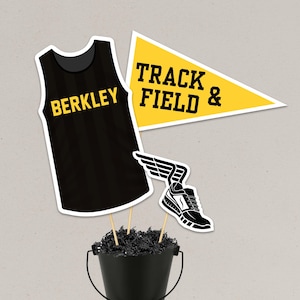 May include: A black and yellow track and field-themed centerpiece. The centerpiece includes a black tank top with "BERKLEY" in yellow, a yellow pennant with "TRACK FIELD &" in black, and a black and white running shoe with wings.