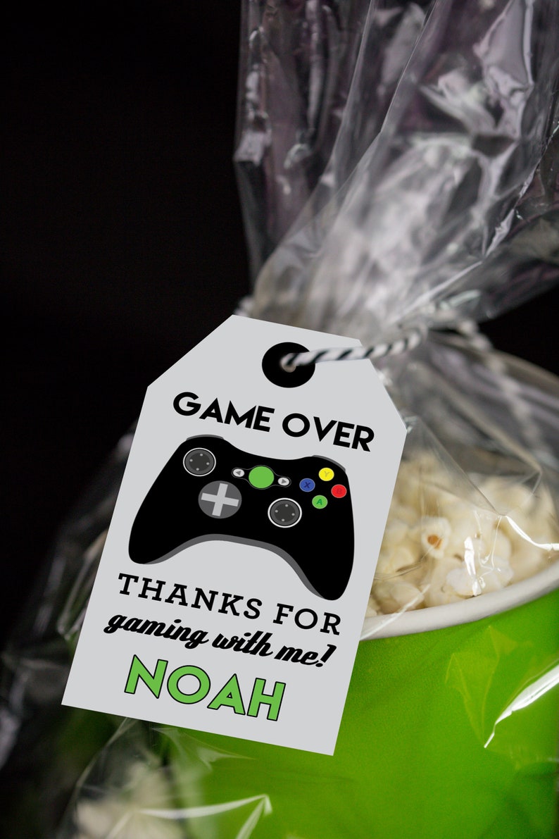 May include: A white favor tag with black and green text that reads "GAME OVER" and features a black video game controller with green, red, yellow, and blue buttons. The tag also says "THANKS FOR GAMING WITH ME! NOAH".