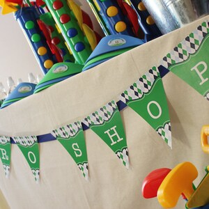 May include: A green and blue banner with the word "PRO SHOP" printed on it. The banner is hanging on a white tablecloth. There are various toys and decorations on the table, including a blue and green golf club set.