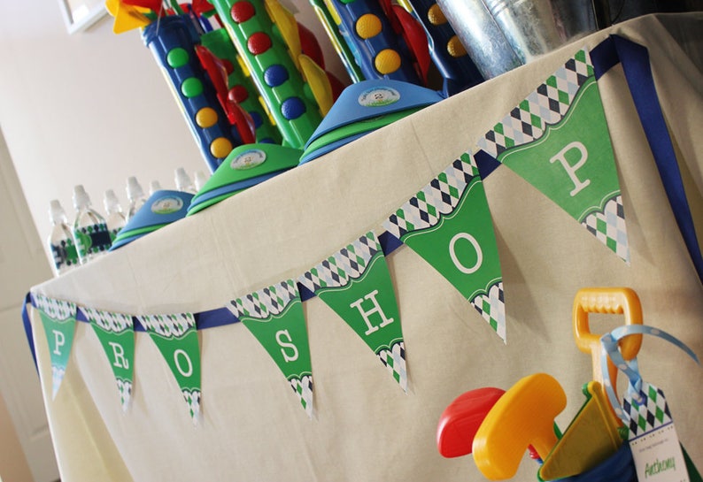 May include: A green and blue banner with the word "PRO SHOP" printed on it. The banner is hanging on a white tablecloth. There are various toys and decorations on the table, including a blue and green golf club set.