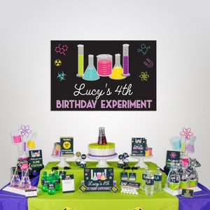 May include: A science-themed birthday party table setting with a black chalkboard sign that says "Lucy's 4th Birthday Experiment". The table is decorated with colorful beakers, test tubes, and other science-themed decorations. There is a cake with a green beaker on top, cupcakes with science-themed toppers, and a variety of other treats.