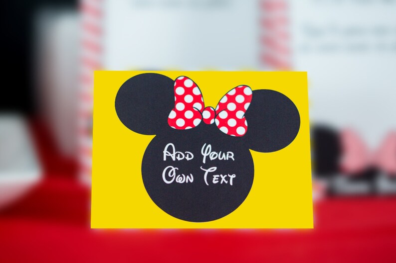 Peut inclure: Une carte jaune avec une silhouette noire de la t&ecirc;te de Minnie Mouse avec un n&oelig;ud rouge &agrave; pois blancs. Le texte "Add your own text" est &eacute;crit en blanc &agrave; l'int&eacute;rieur de la silhouette.