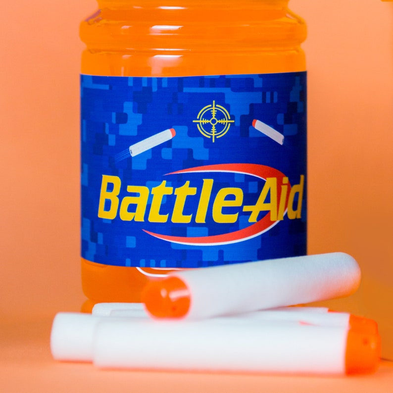 May include: Orange and blue can with the words "Battle-Aid" on the label. The can is surrounded by white foam darts.