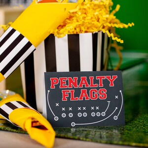 May include: Black and white striped paper cones filled with yellow shredded paper. A sign reads "Penalty Flags" with a football field diagram.