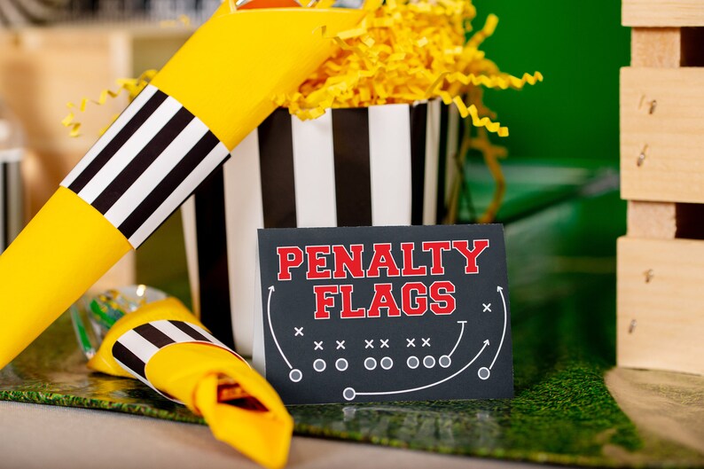May include: Black and white striped paper cones filled with yellow shredded paper. A sign reads "Penalty Flags" with a football field diagram.