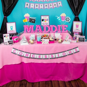 May include: A pink and black movie-themed party table with a banner that says "CONCESSIONS" and a sign that says "Maddie's Movie Night". There are various decorations, including popcorn, film reels, and a sign that says "Happy 8th Birthday".