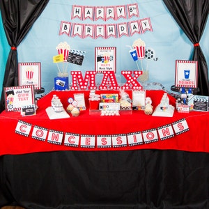 May include: A movie-themed birthday party setup with a red and black color scheme. The table is decorated with popcorn, film reels, and signs that say "Happy 8th Birthday", "Concessions", and "Max's Movie Night".