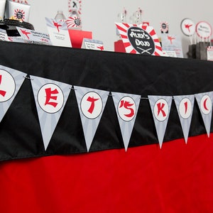 May include: A black and red table with a banner that says "Let's Kick It" in white letters on a gray background. The banner is made of triangular flags with a white circle in the center of each flag.