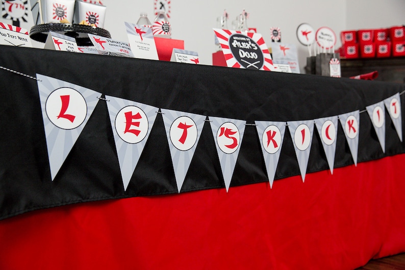May include: A black and red table with a banner that says "Let's Kick It" in white letters on a gray background. The banner is made of triangular flags with a white circle in the center of each flag.