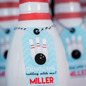 May include: White ceramic bowling pin party favors with blue and white chevron patterned tags. The tags have a black and white bowling ball and pins graphic and the text "Thanks for rolling with me! MILLER".