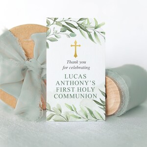 Puede incluir: Una tarjeta blanca con ramas verdes y una cruz dorada. El texto dice "Gracias por celebrar la Primera Comuni&oacute;n de Lucas Anthony".
