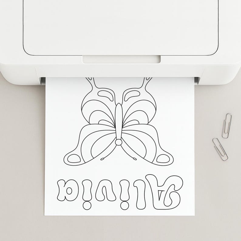 May include: A white sheet of paper emerging from a white printer featuring a black line art drawing of a butterfly and the name Alivia written in a stylised bubble font. Two silver metal paper clips are positioned to the right of the paper.