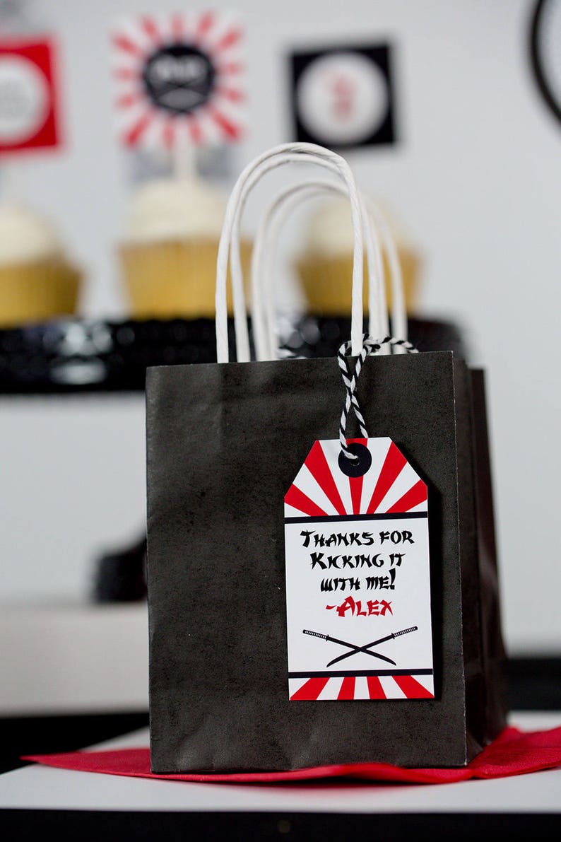 May include: Black and red party favor bag with a white handle and a red and white tag that says "Thanks for kicking it with me! -Alex".