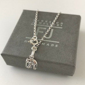 May include: A silver chain necklace with a small silver elephant charm. The necklace is in a grey box with the text "FUNKSON JEWELLERY HANDMADE".