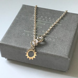 May include: A silver chain necklace with a small sun charm. The necklace is in a grey box with the text "FUNKS JEWELLERY HANDMADE".