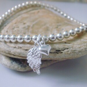 May include: A silver beaded bracelet with a charm featuring an angel wing and a heart.