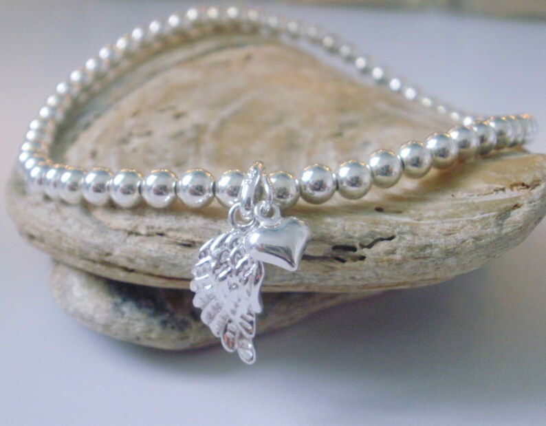 May include: A silver beaded bracelet with a charm featuring an angel wing and a heart.