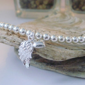 May include: A silver bracelet with a small silver heart and angel wing charm. The bracelet is made of small silver beads.