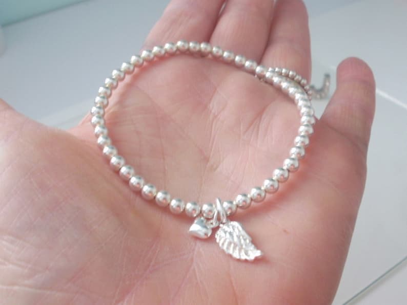 May include: A silver beaded bracelet with a small silver heart and angel wing charm.