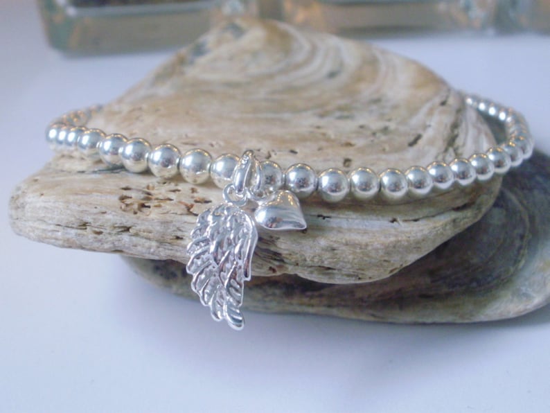 May include: A silver beaded bracelet with a charm featuring an angel wing and a heart.