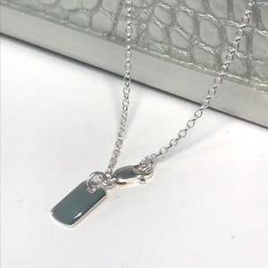 May include: A silver chain necklace with a small, rectangular tag pendant.