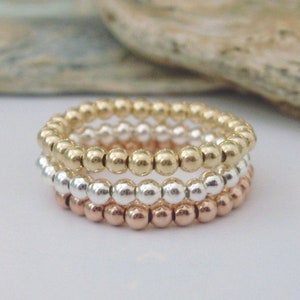 May include: Three stacked rings made of gold, silver, and rose gold beads.