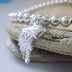 May include: A silver bracelet with a charm of a heart and a wing. The bracelet is made of small silver beads.