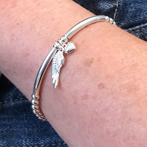 Può includere: Un braccialetto rigido in argento con un piccolo ciondolo a forma di cuore in argento e un ciondolo a forma di ala d'angelo in argento.