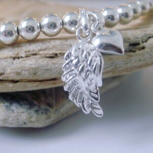 May include: A silver charm bracelet with a heart and angel wing charm. The bracelet is made of small silver beads.