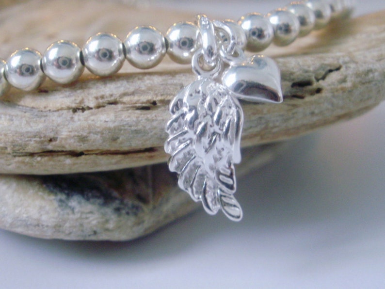 May include: A silver charm bracelet with a heart and angel wing charm. The bracelet is made of small silver beads.