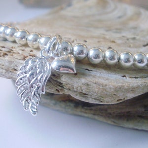 May include: A silver beaded bracelet with a silver angel wing charm and a silver heart charm.