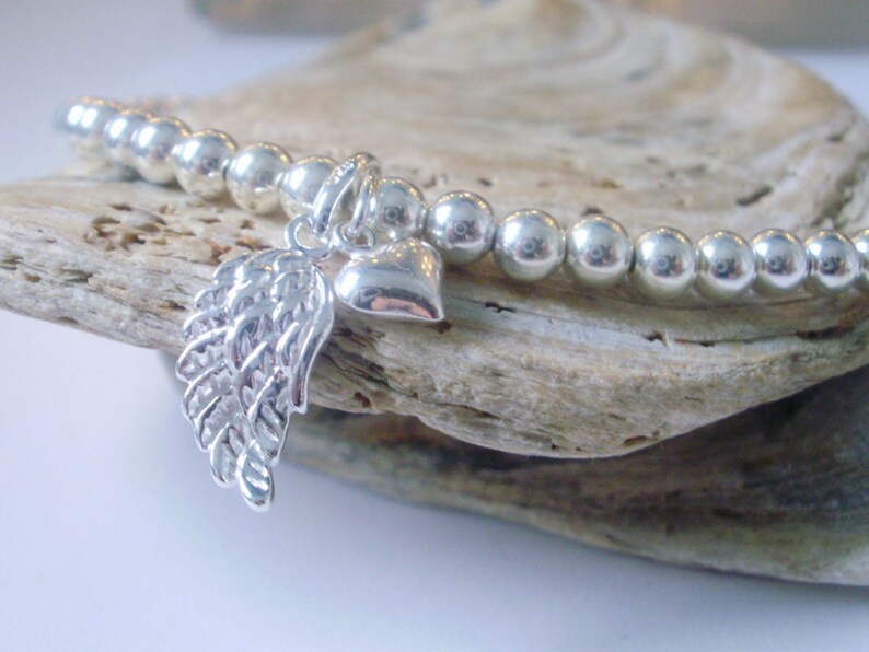 May include: A silver beaded bracelet with a silver angel wing charm and a silver heart charm.