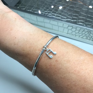 May include: A silver bracelet with a music note charm. The bracelet is made of small beads and has a simple, elegant design.