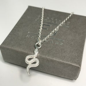 May include: A silver snake pendant necklace on a silver chain. The necklace is in a grey box with the word "Handmade" printed on it.