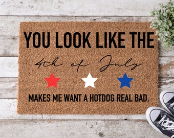 Op de afbeelding: Een bruine deurmat met de tekst "YOU LOOK LIKE THE 4th of July MAKES ME WANT A HOTDOG REAL BAD." De tekst is in zwart met rode, witte en blauwe sterren.