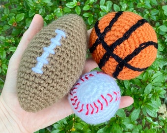 May include: Three crocheted balls, one brown and white football, one orange and black basketball, and one white baseball with red stitching.