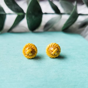 Op de afbeelding: Een paar gele miniatuur taart oorbellen. De oorbellen zijn gevormd als een taartkorst met een bruine vulling.
