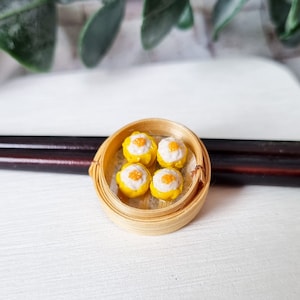 Op de afbeelding: Vier gele en witte dim sum dumplings in een ronde bamboe stoommandje.