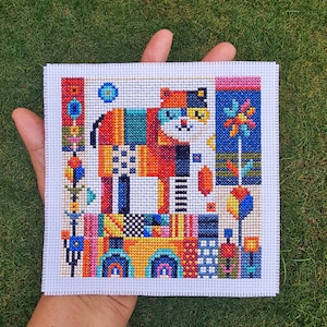 May include: A colorful cross-stitch pattern of a cat with geometric shapes and a floral design. The cat is made up of various colors, including red, orange, yellow, green, blue, and black. The background is white.