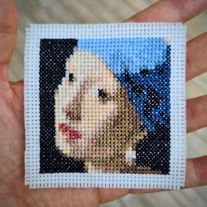 Puede incluir: Bordado de punto de cruz de un retrato de una mujer con un pañuelo azul. El rostro de la mujer es parcialmente visible y mira hacia la izquierda. El fondo es negro.