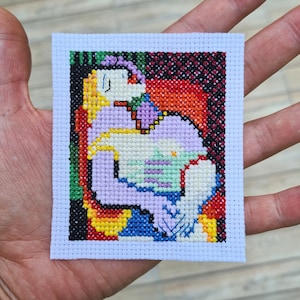 Puede incluir: Bordado de punto de cruz que representa un retrato abstracto colorido de una persona sobre un fondo morado, amarillo y verde.