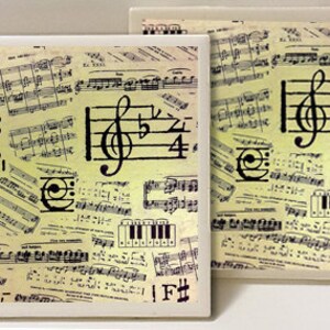 May include: Two square ceramic coasters with a vintage music sheet design. The coasters feature a treble clef, musical notes, and piano keys. The background is a light yellow with black musical notes.