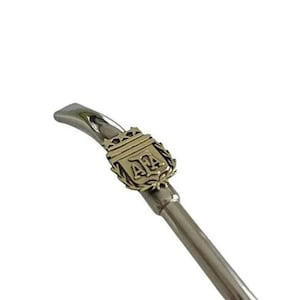 Puede incluir: Una bombilla de metal plateado con un emblema dorado que presenta las letras "AFA" rodeadas de una corona.