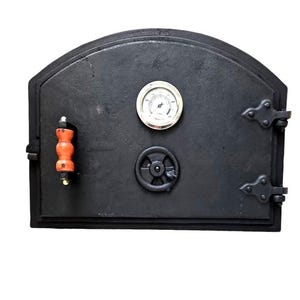 May include: A black cast iron oven door with an arched top, featuring a circular analogue thermometer, a small round air vent dial, and a vertical handle with a reddish-brown wooden grip. The door is attached with two decorative metal hinges.