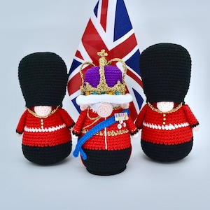 Puede incluir: Tres figuras de crochet de guardias británicos, uno con una corona y una túnica morada, de pie frente a una bandera de la Union Jack.