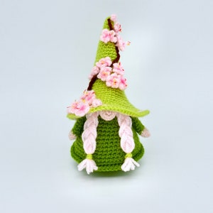Peut inclure: Un gnome crocheté vert avec des cheveux en laine rose et un chapeau décoré de fleurs crochetées roses.